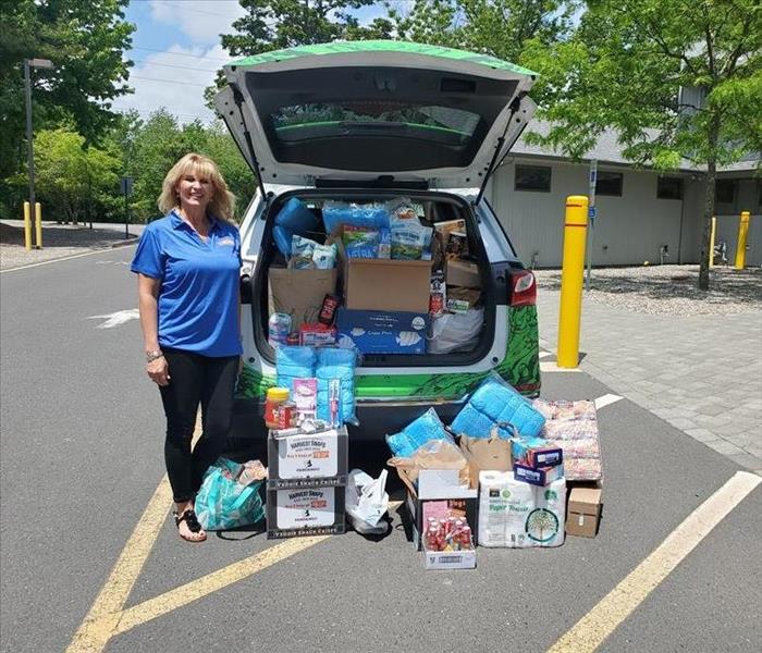 Kathy standing next to SERVPRO of Point Pleasant with car full of food and personal items that were donated
