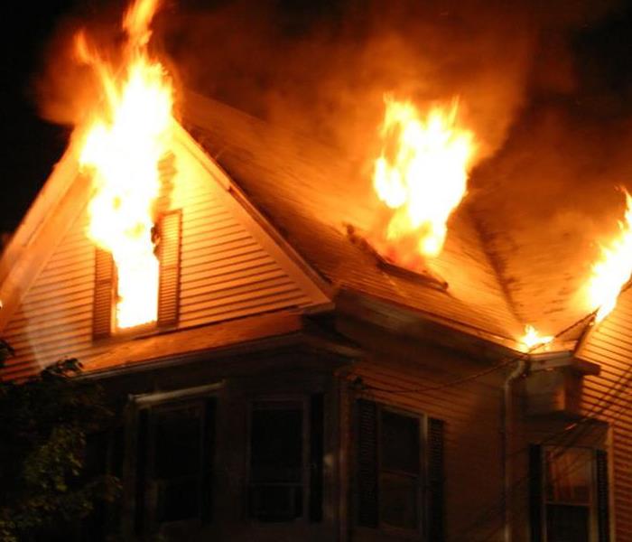 A home with a fire burning out windows at night. 