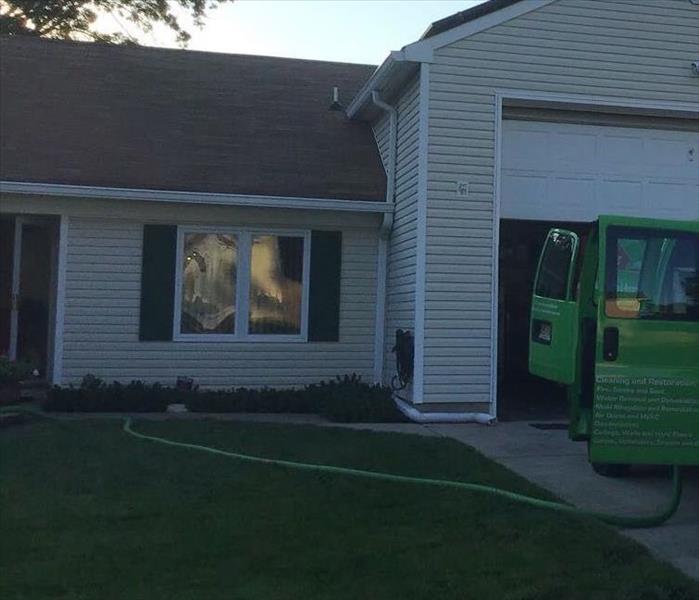A SERVPRO vehicle in front of a home with hoses going into the home. 